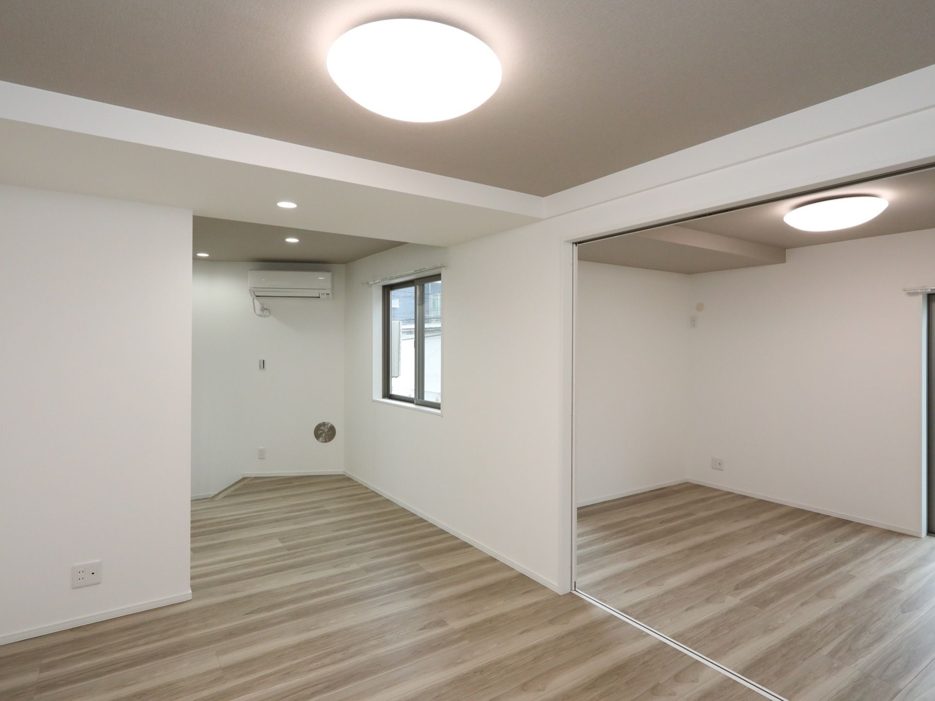 白い壁紙で、床は木目調である。部屋の隅に窓があり、その近くにはエアコンが取り付けられている。天井はグレーで塗られている。