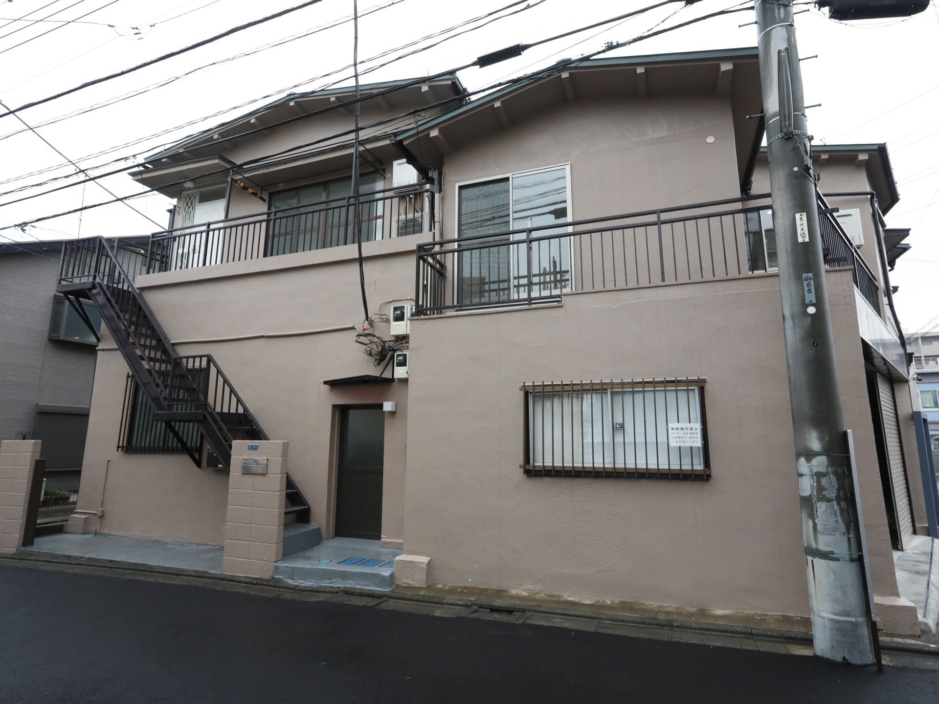 ２階のベランダから、外階段を使って玄関まで下りることができる。建物は道路に隣接しており、間にはブロック塀がある。