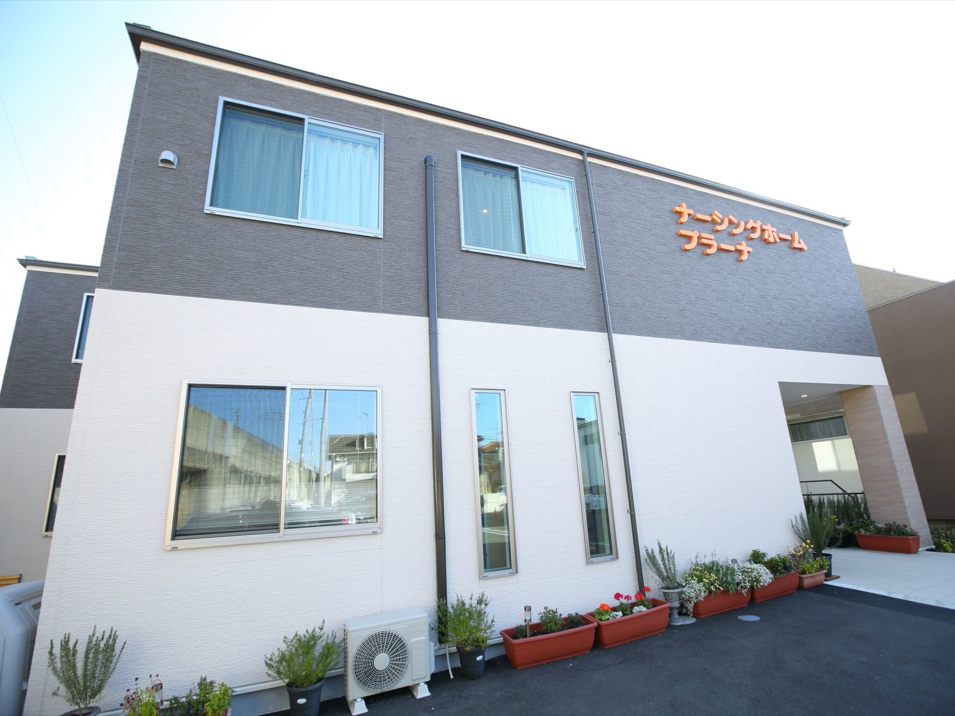 ２階建てで、色は白とグレーの二層で構成されており、落ち着きのあるモダンな外観となっている。壁に沿ってプランターが並び緑もある。