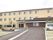 3階建ての建物はクリーム色で大きく、敷地内には駐車場もあり、車が数台止められている。玄関には車寄せが付いている。