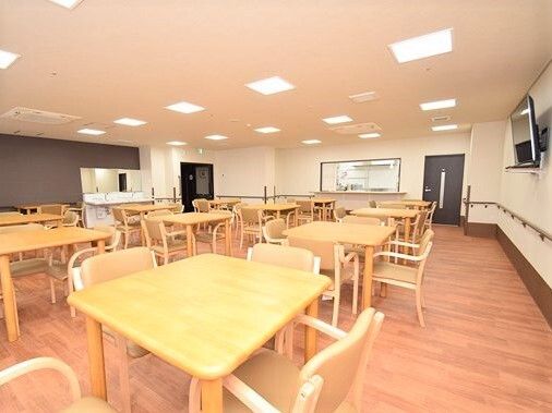 食堂からは厨房内を見ることができるよう大き目の窓が設置されている。木製の少人数向けのダイニングテーブルがたくさん並び、壁掛けテレビもある。
