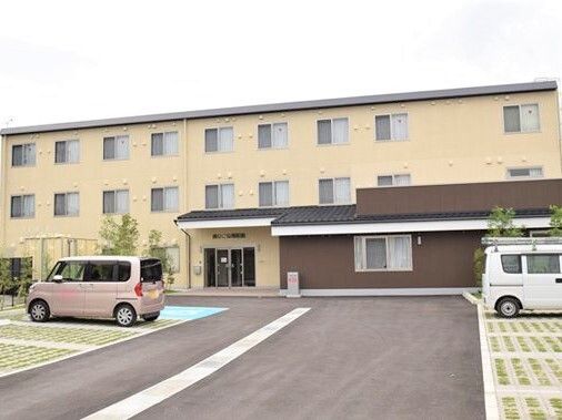 3階建ての建物にはたくさんの窓が付き、広い敷地内には駐車場も完備され、数台の車が止められている。クリーム色で明るい雰囲気。