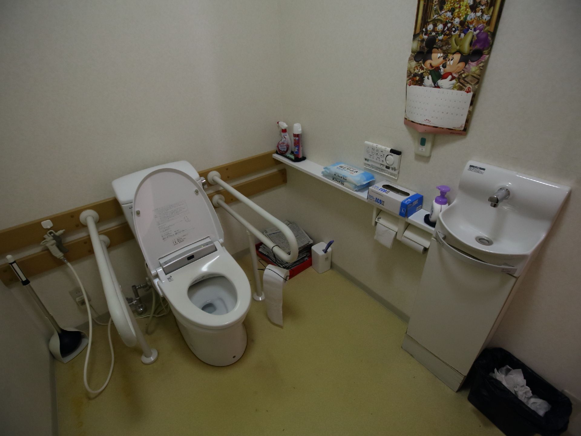 便器の両側に手すりが設置され、手洗器や棚が付いた広いトイレ