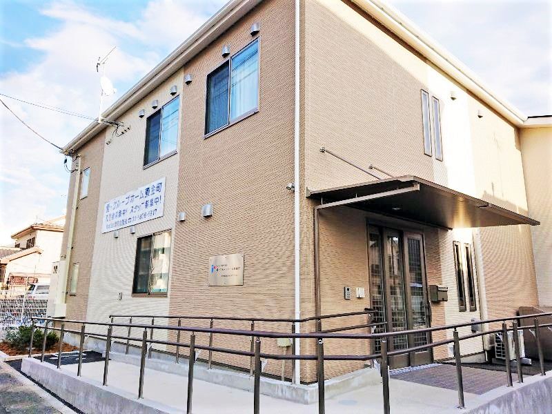 ブラウン系の2階建ての建物は住宅地にあり、外壁にはホーム名が書かれ、玄関先にはスロープが付いている。