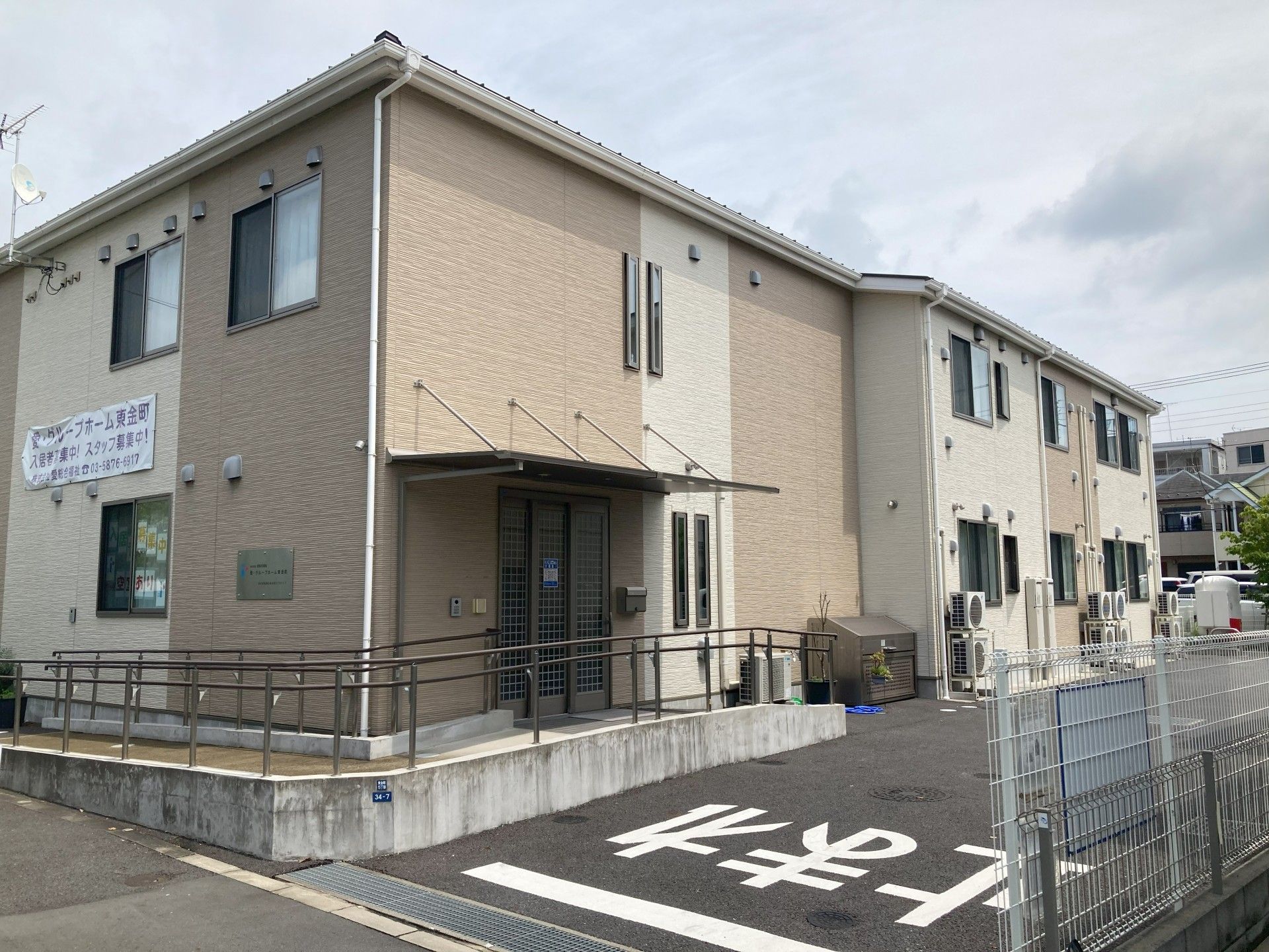 ブラウン系の2階建ての建物。玄関部分には屋根があり、スロープも付いている。