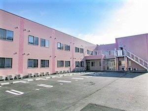 鉄骨造２階建ての建物の外観写真。手前に駐車場スペースがある様子