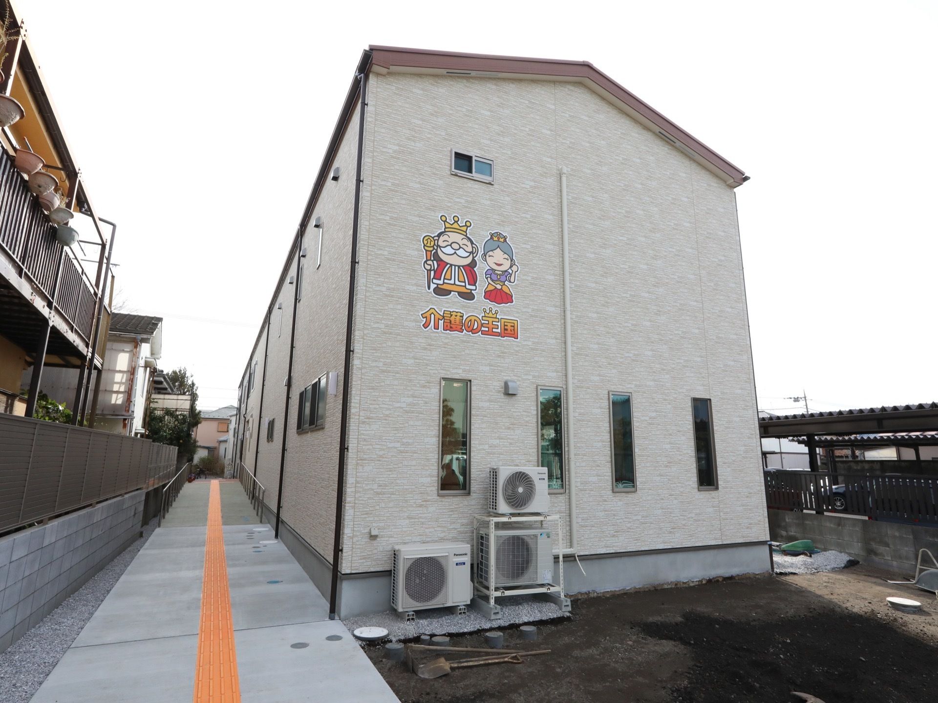 施設は公道に面している。隣地との間に、点字ブロックを敷いた通路が設置されている。建物の壁には、施設名称が入っている。