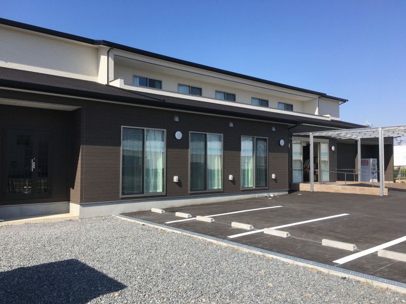 ２階建ての建物は白とブラウンで駐車スペースも付き、玄関には手すり付きのスロープがある。