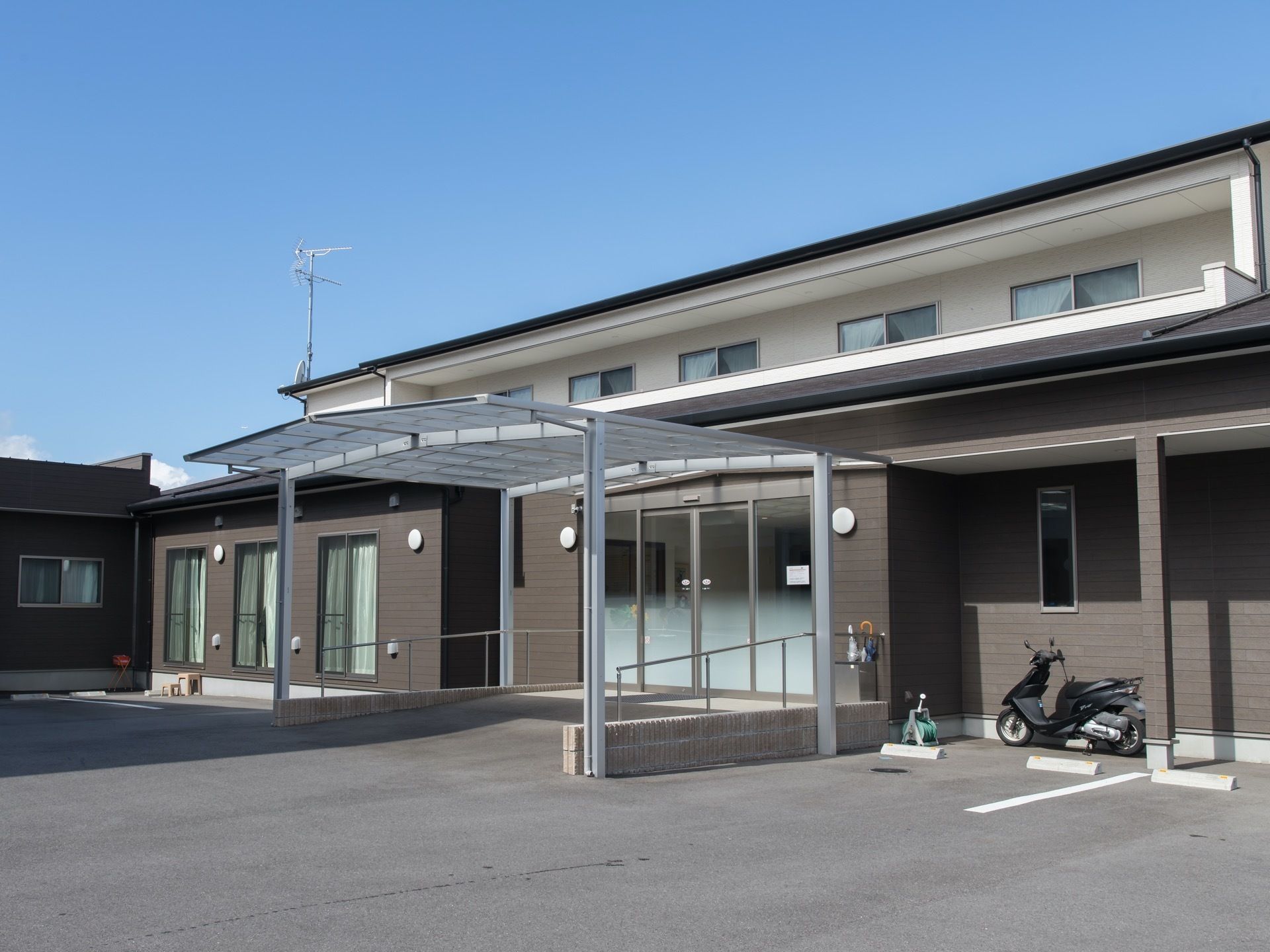 現代風のデザインで、グレーと白色の外壁をした建物がある。建物の玄関の近くには駐車スペースが設けられている。