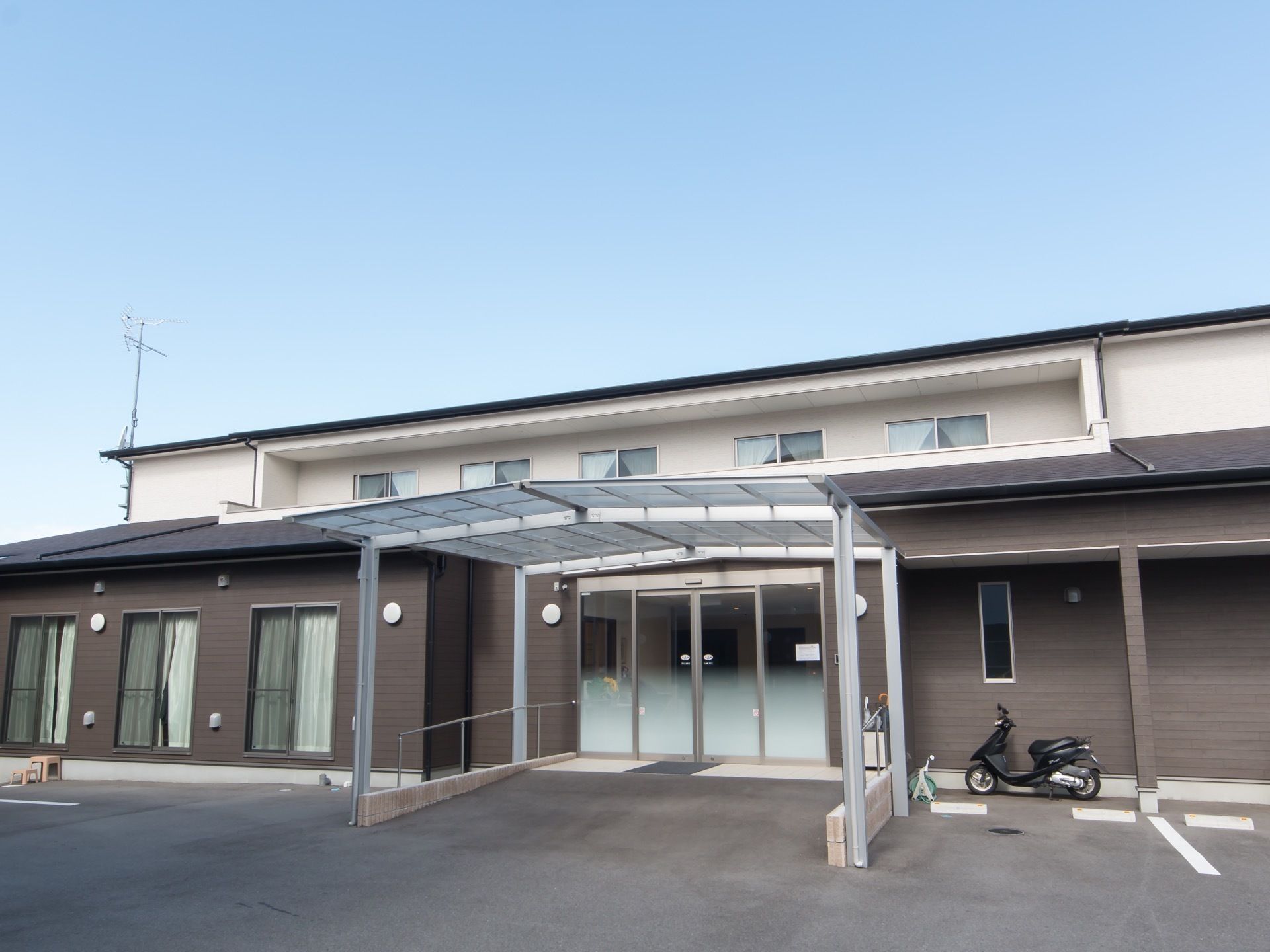 グレーと白を基調とした2階建ての建物が建っている。建物の玄関の前にはスロープがあり、その上にひさしが設けられている。
