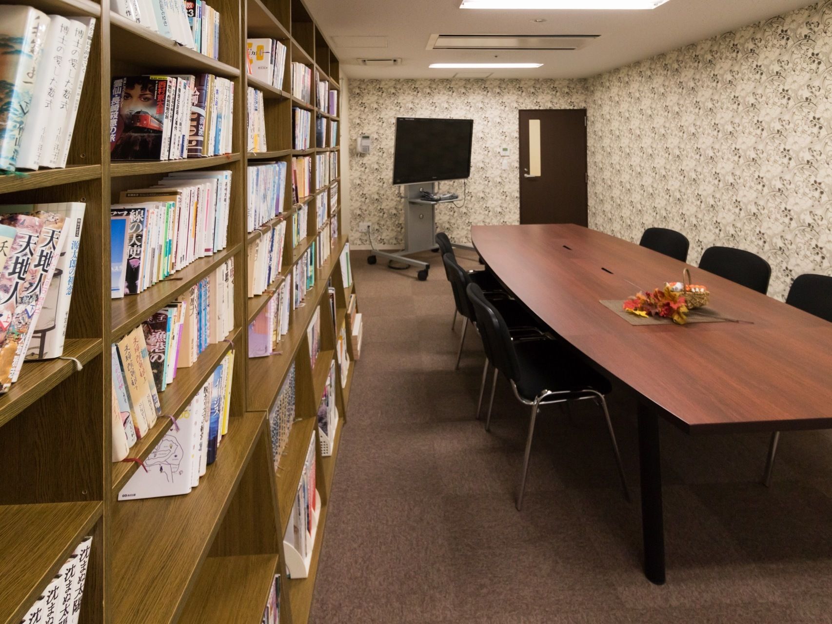 カーペット敷きの部屋に、長机と椅子が置かれている。壁際には大きな本棚があり、雑誌や小説がたくさん並べられている。