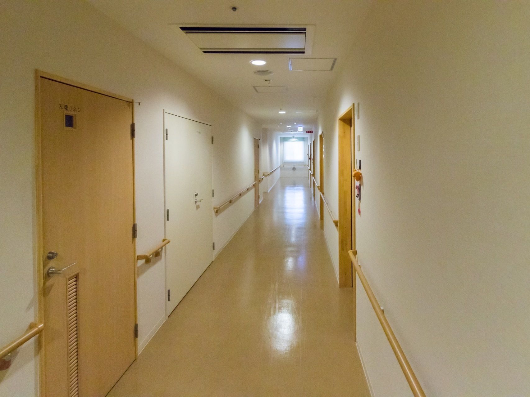 手すりのついた長い廊下が続いていて、片側には居室の入口が並んでいる。空調や防火扉が備えつけられている。