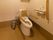 共用のトイレは、車椅子でも余裕をもって利用できる広さがある。便座の両脇に手すりがあり、クッションのついた背もたれもある。