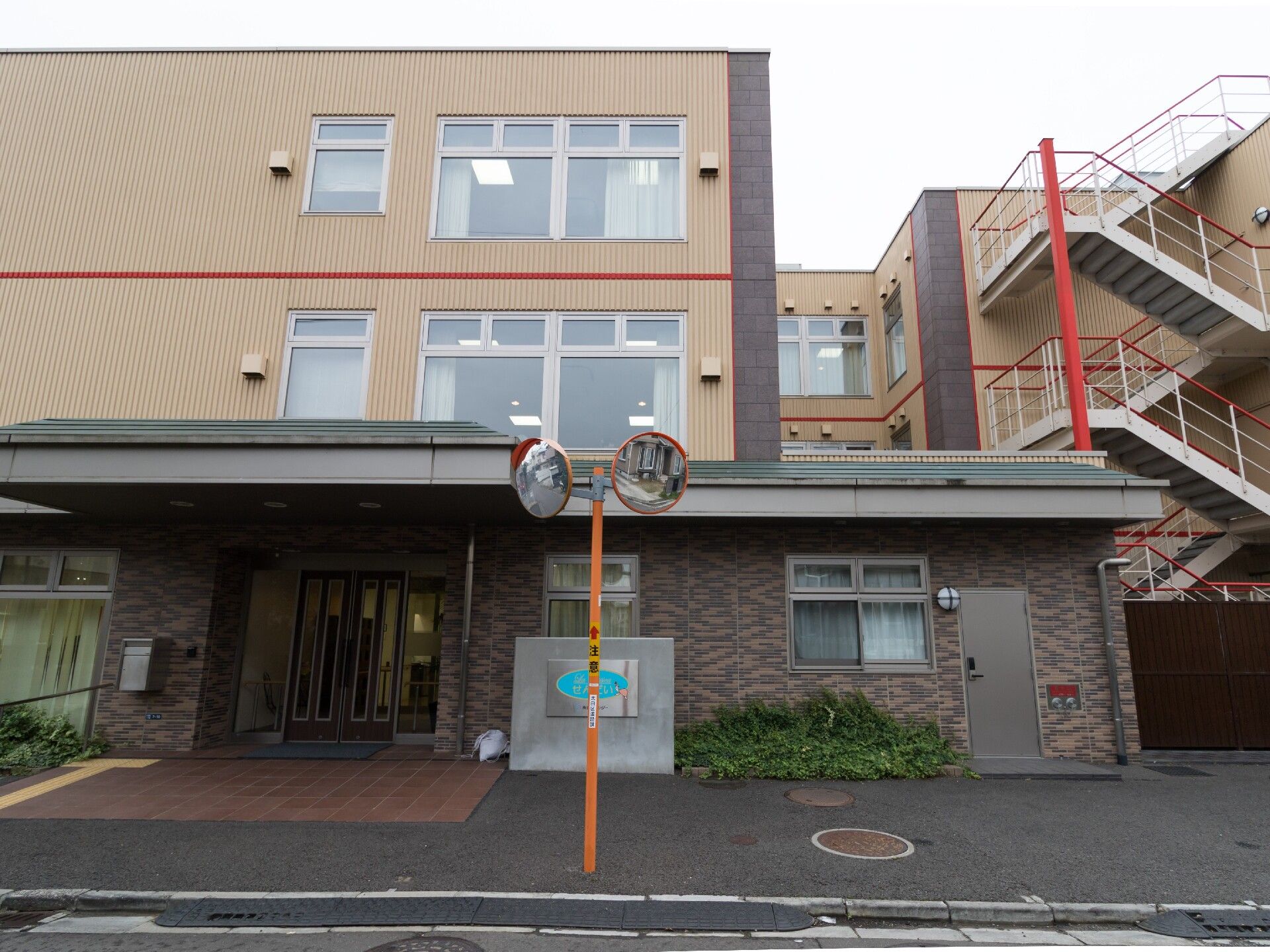 ガラス張りの玄関には雨除けの張り出し屋根が設置され、石畳があるエントランス側の外観