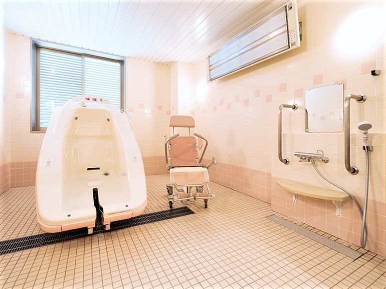 ピンクのタイルが貼られた浴室には機械浴が設置され、換気用の大きな窓もあり、手すり付きのシャワーもついている。