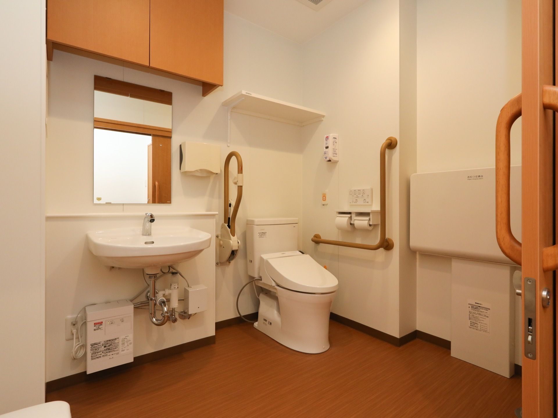 洗面台が備えつけられている広々とした個室トイレである。便器の両サイドには手すりが設置されており、スライド式の扉で仕切られている。