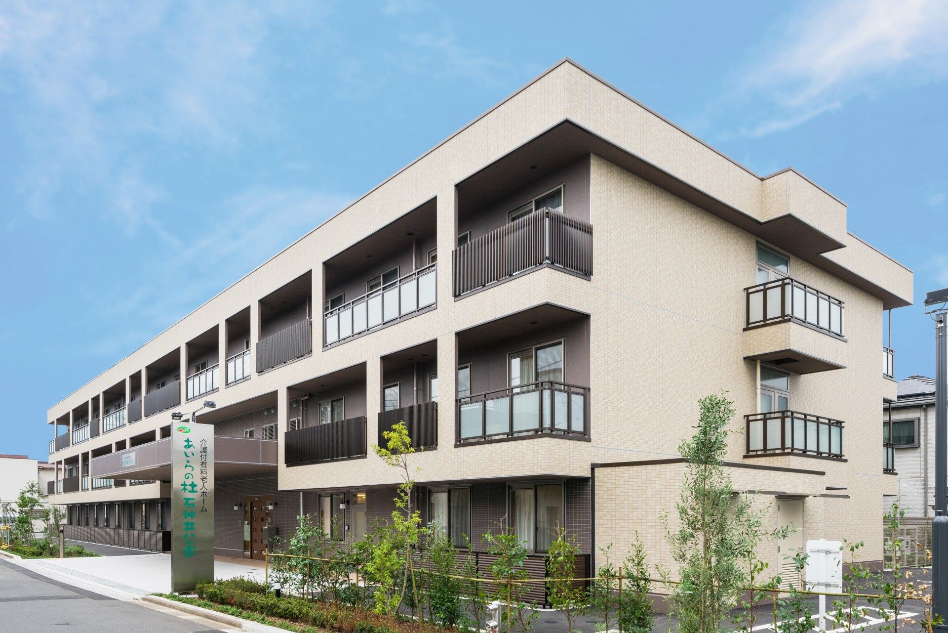3階建ての建物は各フロアにベランダが付き、屋外には階段もあり、周辺には緑が植えられている。