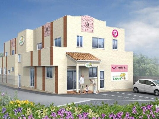 ２階建ての建物はベージュ系で玄関に屋根があり、駐車場には車が止まっている。玄関には高齢者と子供がいる。