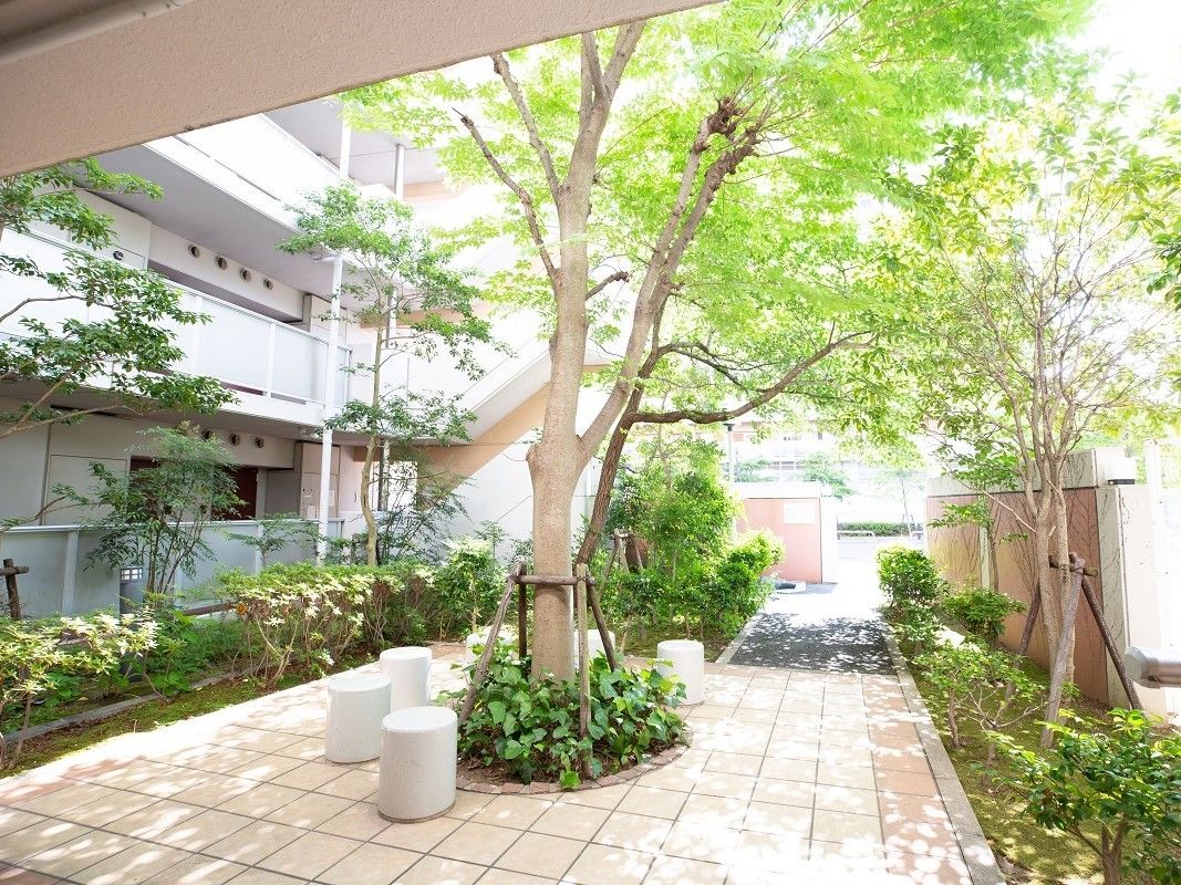 大きな木が生えた木陰が気持ちよさそうな施設の中庭。石でできた椅子が置いてある様子