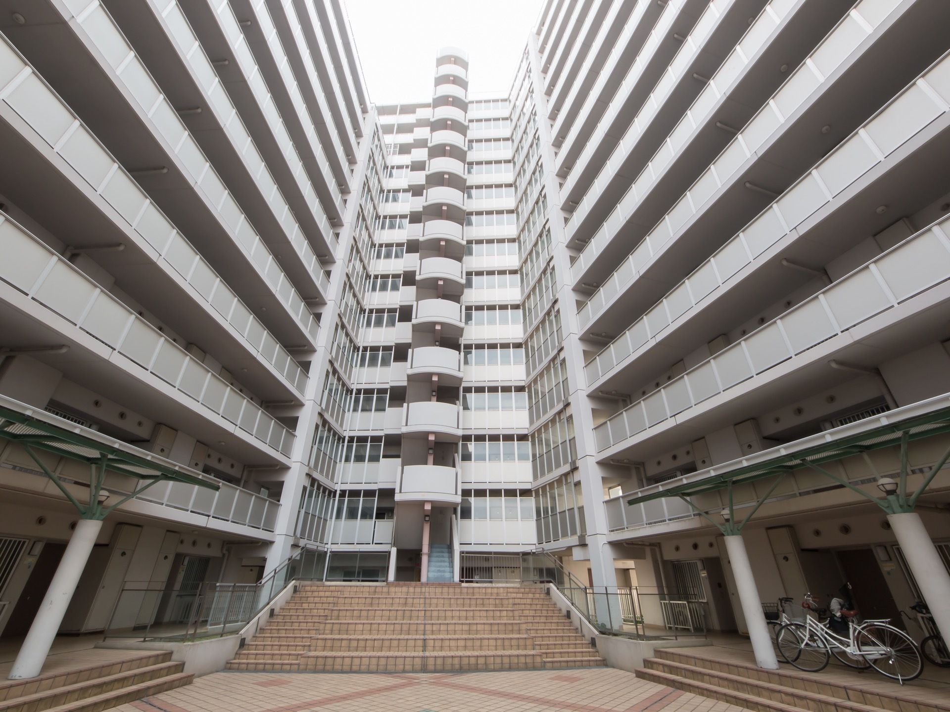 マンションの中庭スペース。正面に最上階まで続く階段が設けられている。手前の両側には屋根付きの駐輪場がある。