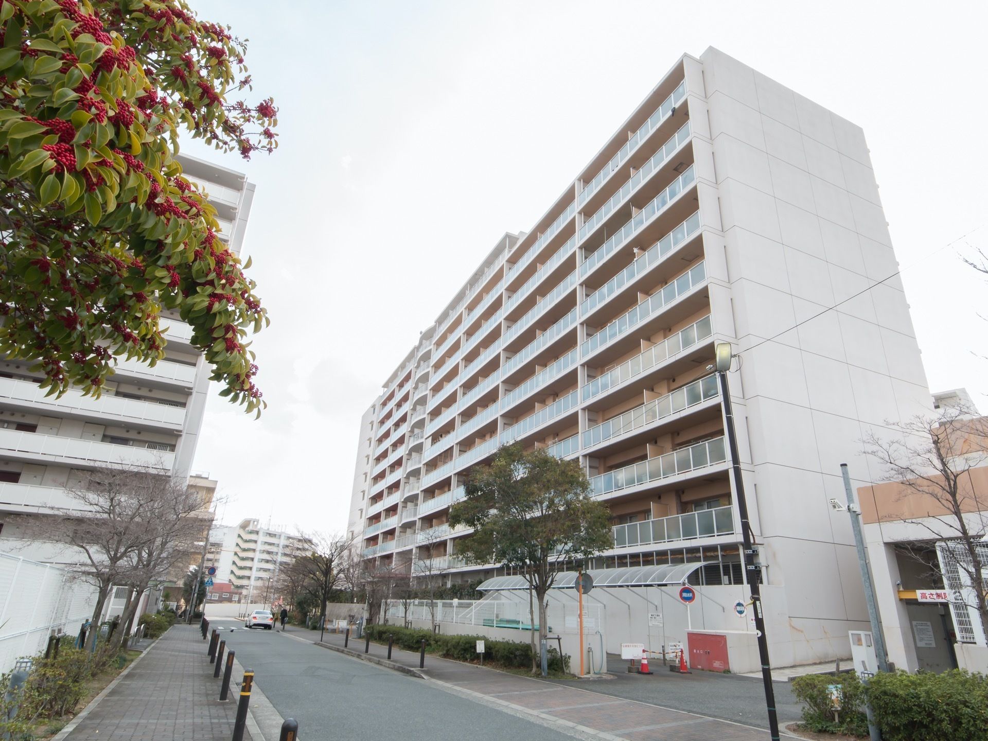 高層の建物があり、その手前に道路が伸びている。歩道が広く取られていて、車道との間にはチェーン状のガードレールが付けられている。