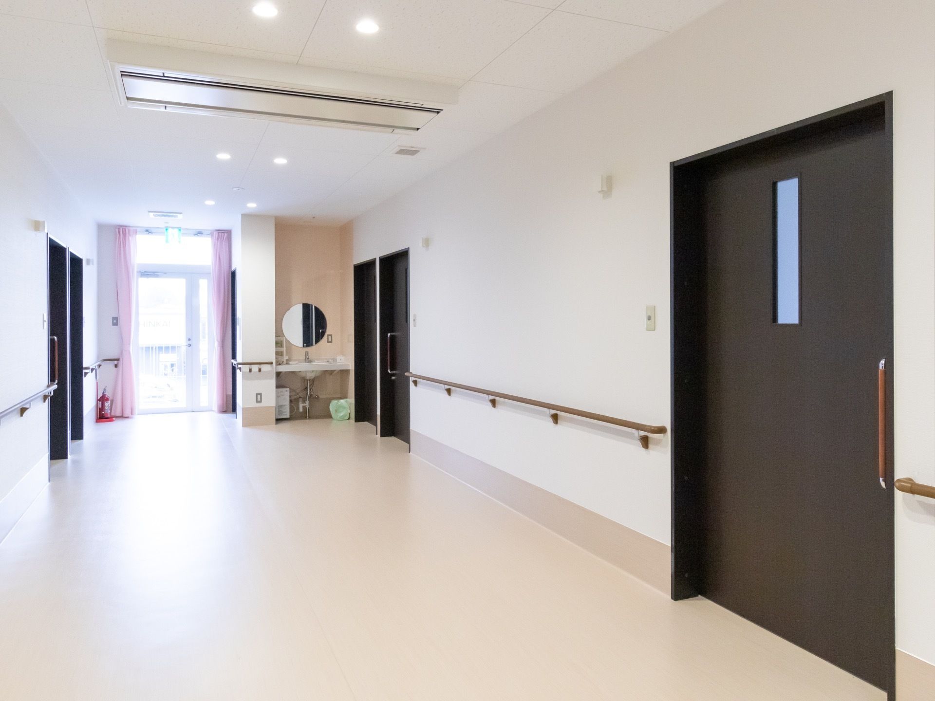 壁に手すりが設置された通路。突きあたりに洗面台が配置されている。