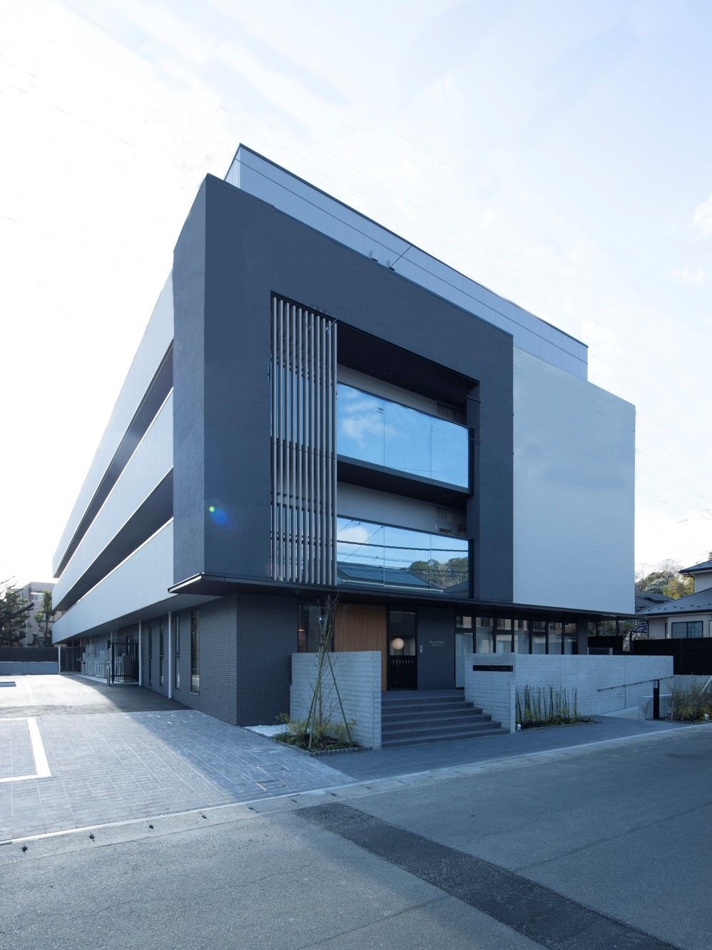 グレー系の4階建ての建物。周辺には木が植えられ、玄関には屋根がある。