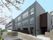 グレーをメインとした重厚感のある建物は3階建てで、桜が咲いている道路に面している。