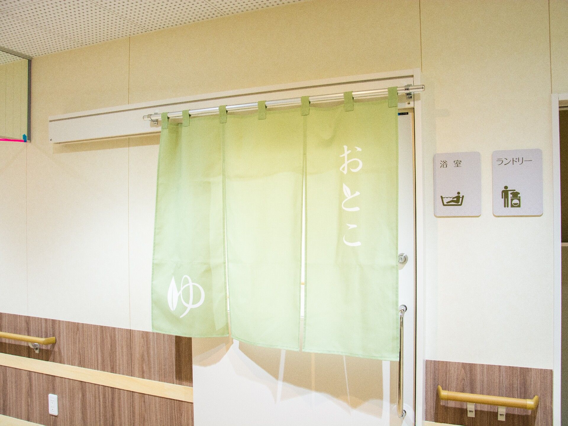 ランドリーの隣にある、さわやかなグリーンの暖簾がかかった男性用浴室の入口