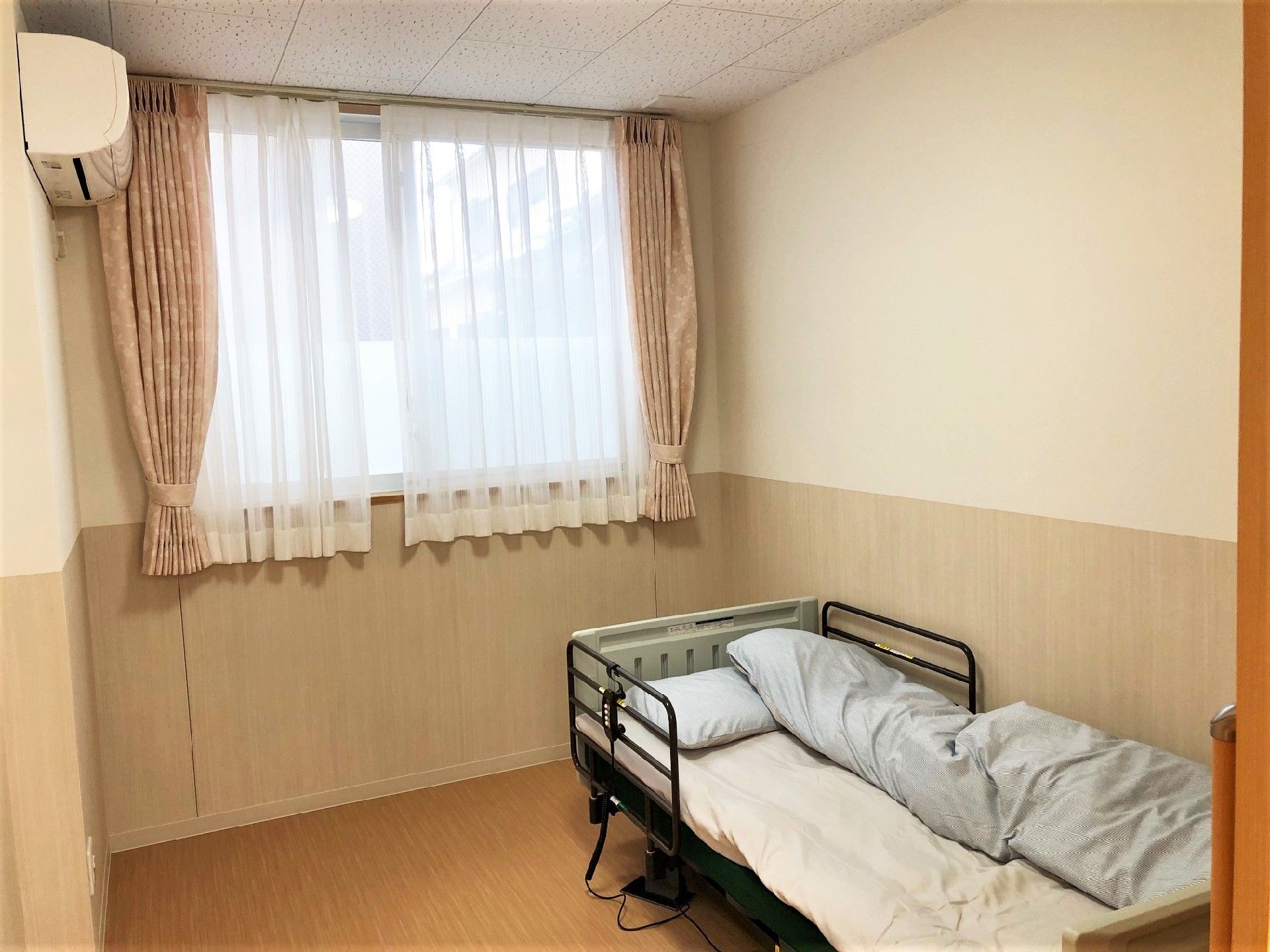 大きな窓がついた個室の部屋には寝具付きのベッドやエアコンがある。