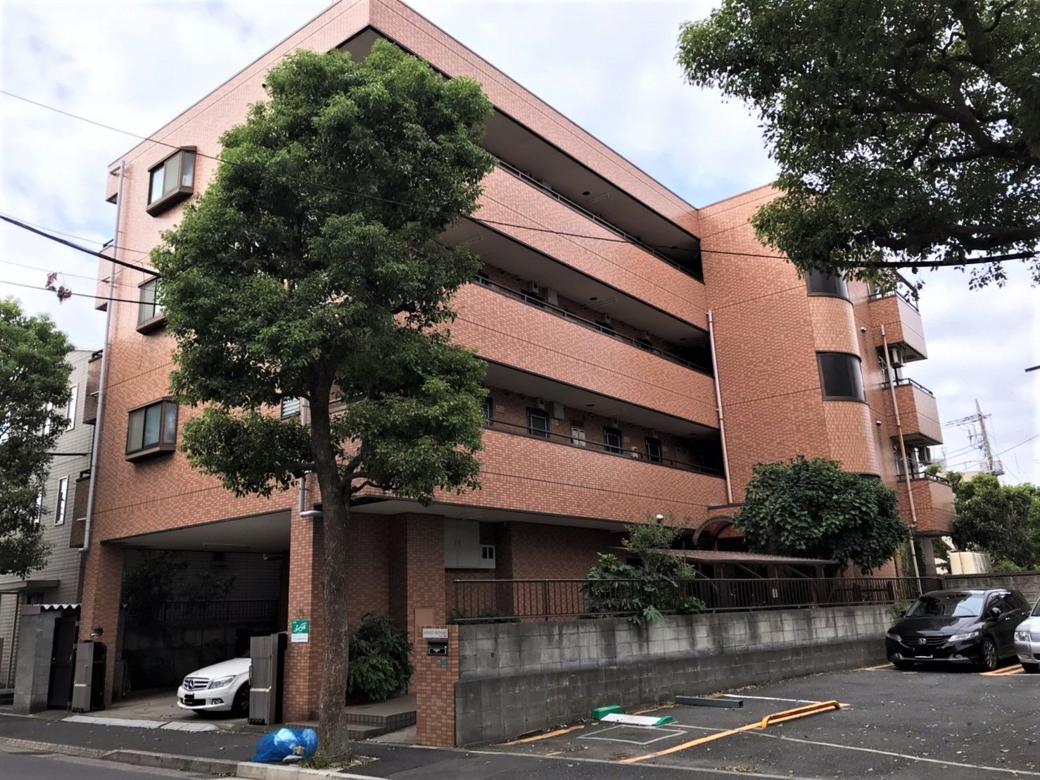 マンション風の鉄骨造の建物の外観。手前に駐車場スペースがある空間