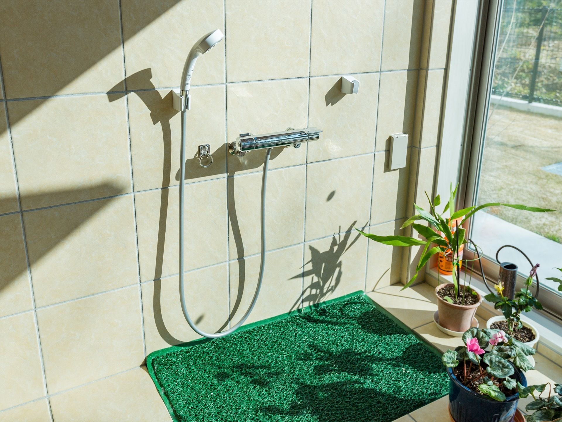 床にはマットが敷かれている。観葉植物や花が置かれている。壁にはリードをつなぐ器具が付けられている。