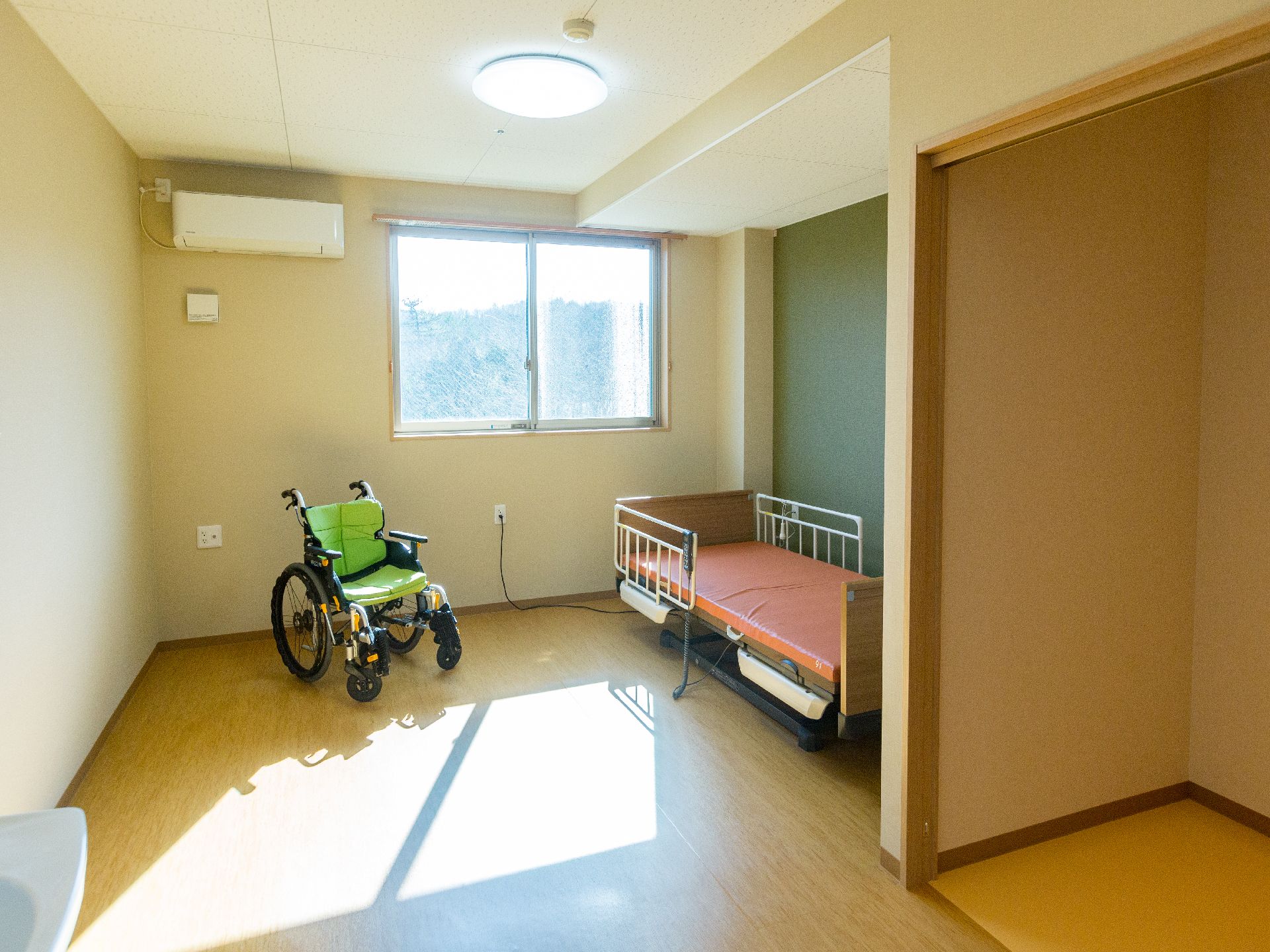 介護機能付きのベッドと黄緑色の車椅子が置かれた部屋