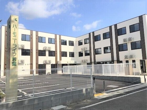 広い駐車場があり、たくさんの窓が付いた建物。白っぽいの３階建ての建物は明るい雰囲気。