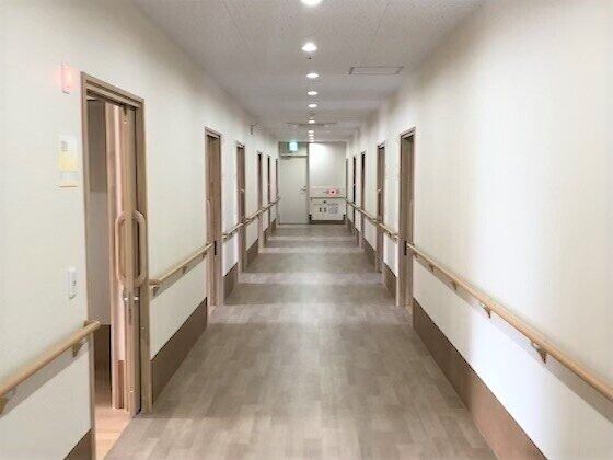 両サイドに居室のドアがあるまっすぐな廊下。突き当りには非常口のサインが付いたドアがある。