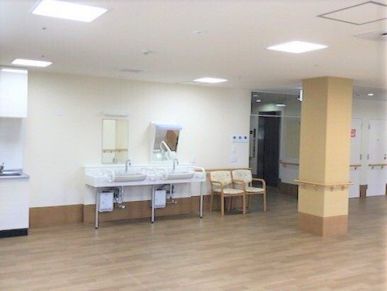 洗面所が二つ並び、その隣にはいすが2脚置かれている。車いす対応のデザインで鏡の一つは斜めに傾けて設置されている。