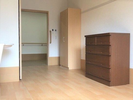 ベージュのフローリングの居室にはブラウンのタンスやベージュのクローゼットが置かれ、日当たり良好。