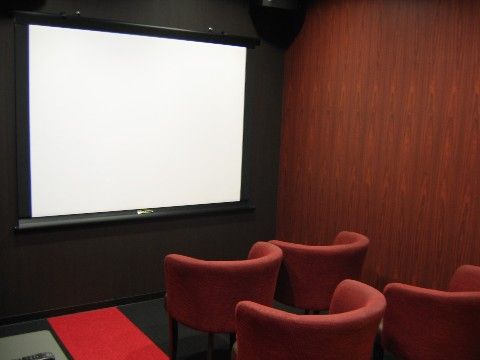 壁面に設置された大きなモニター画面に向かって、椅子が複数並んで置いてあるシアタールーム