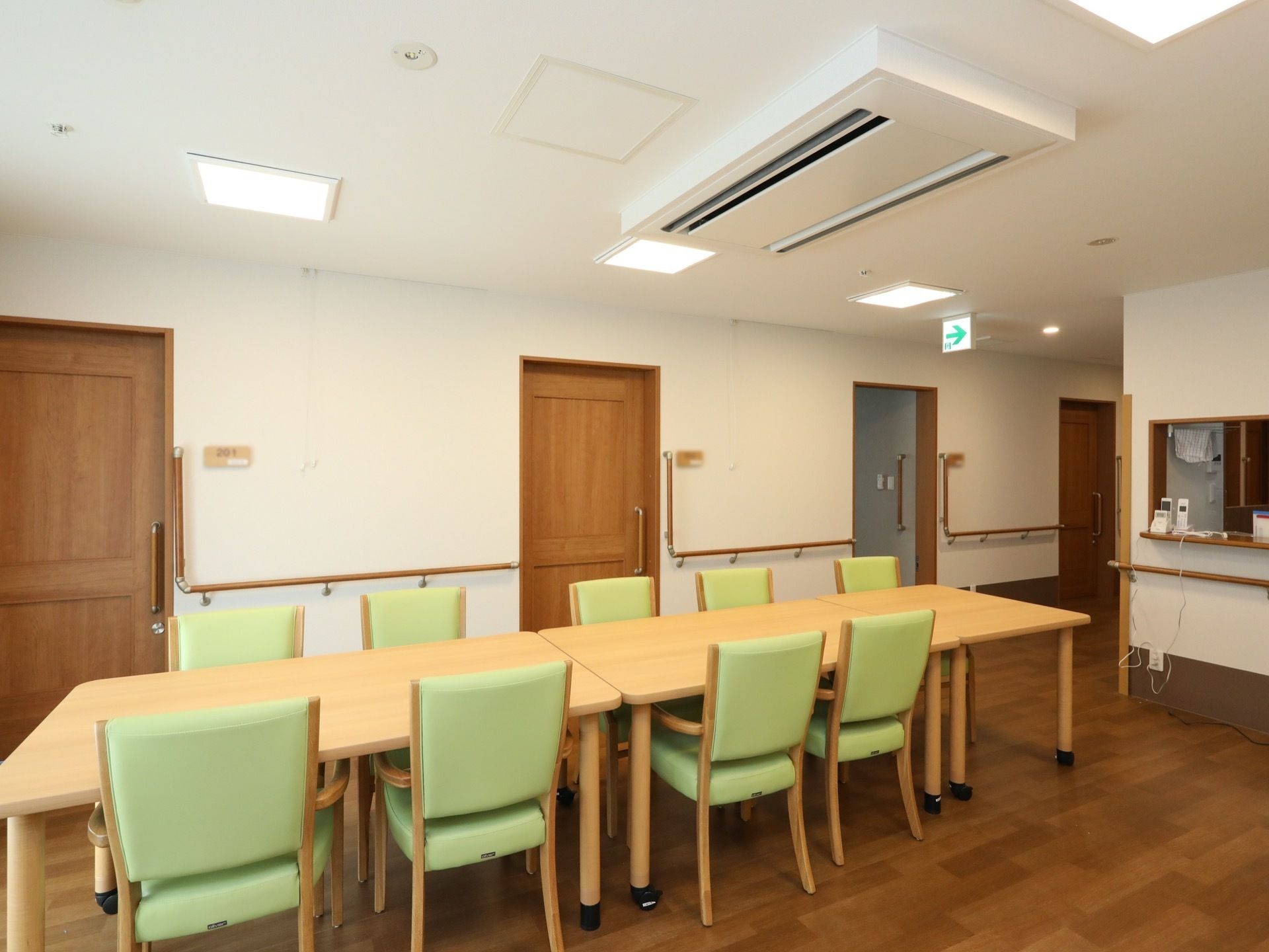 食堂は廊下とつながっていて、居室の前にある。キッチンカウンターがある。天井に横長の吹き出し口があるエアコンが設置されている。