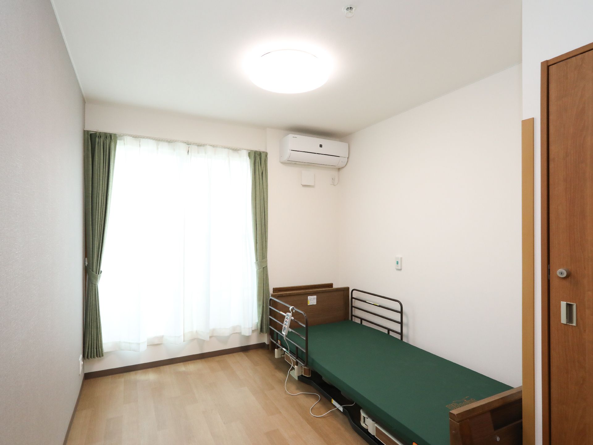 カーテンと介護機能付きベッドの色を緑でそろえた部屋