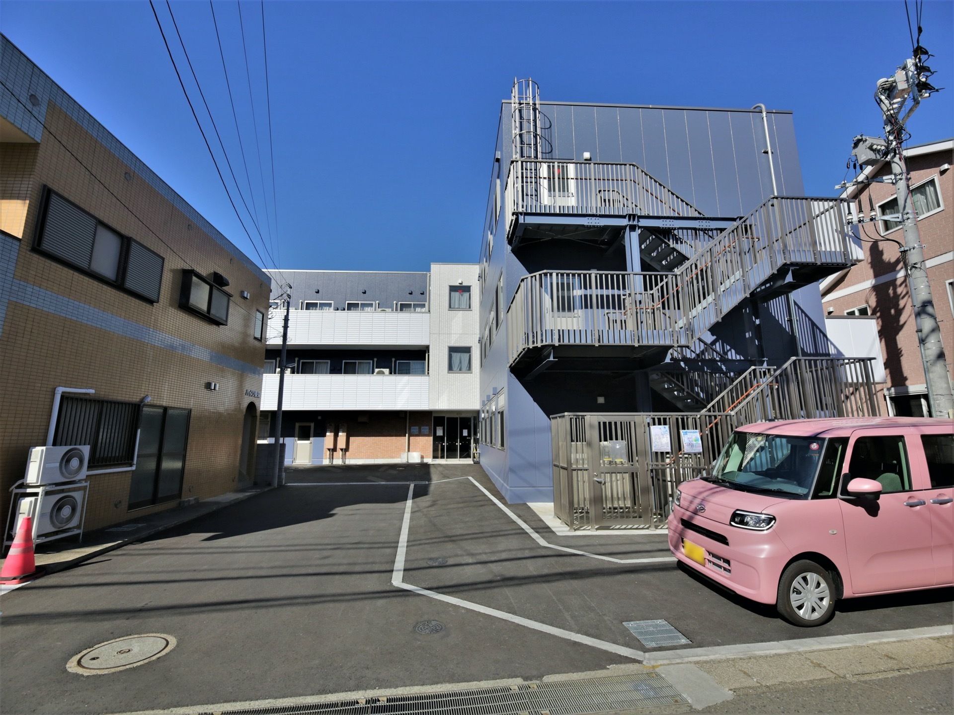 施設はくの字型の３階建てである。外壁はダークグレーでまとめられており、落ち着いた雰囲気となっている。外階段が設置されている。