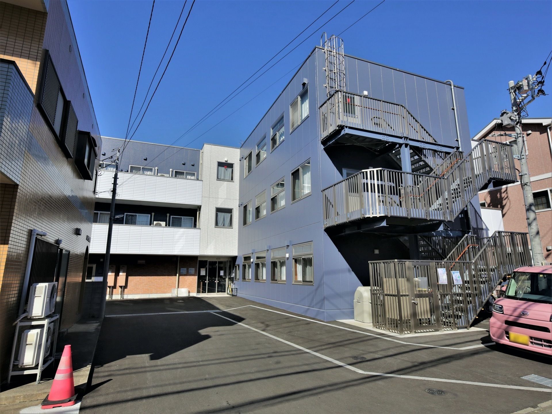 各フロアにベランダが付いた3階建ての建物はダークグレーで道路に面していて、屋外階段も付いている。