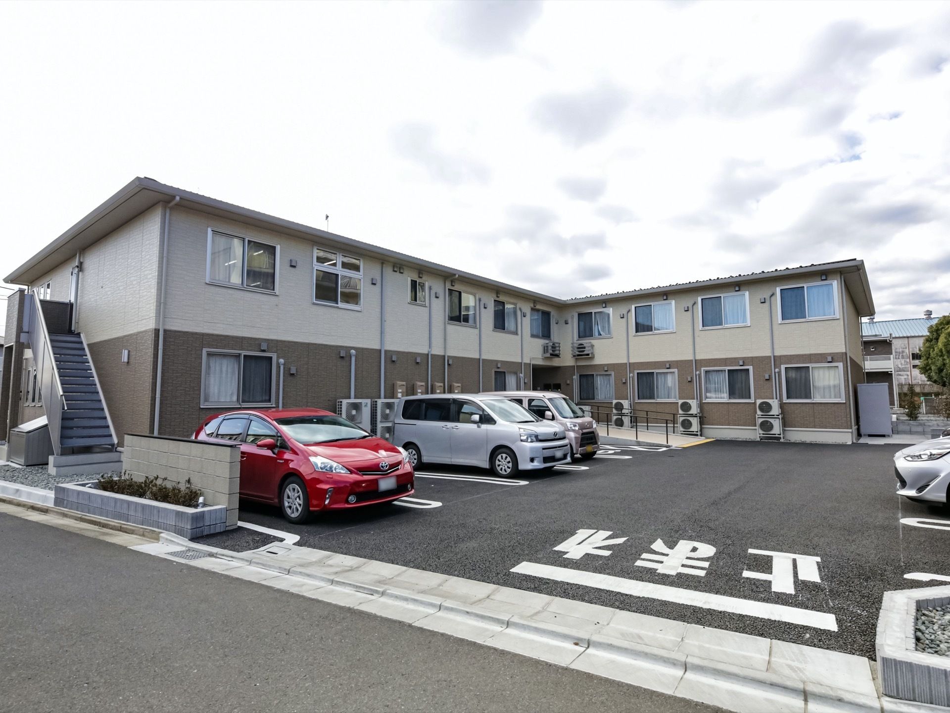 1階部分がブラウン、2階部分がベージュという2階建ての建物。屋外には階段がある。