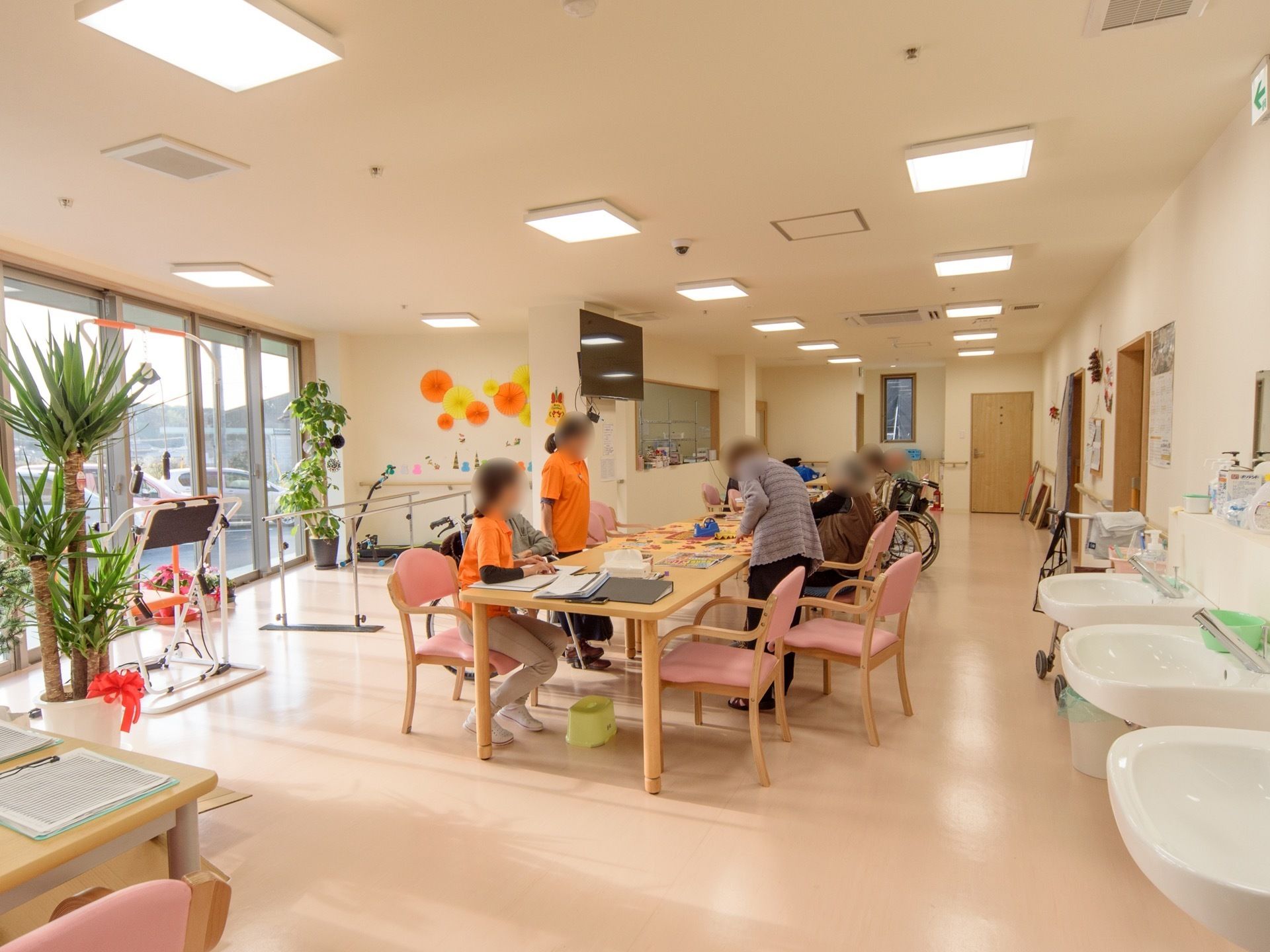食堂ではスタッフと入居者様が趣味の活動を行っている。窓が大きく日当たりに恵まれた空間である。リハビリ専用の機材が窓側に置かれている。