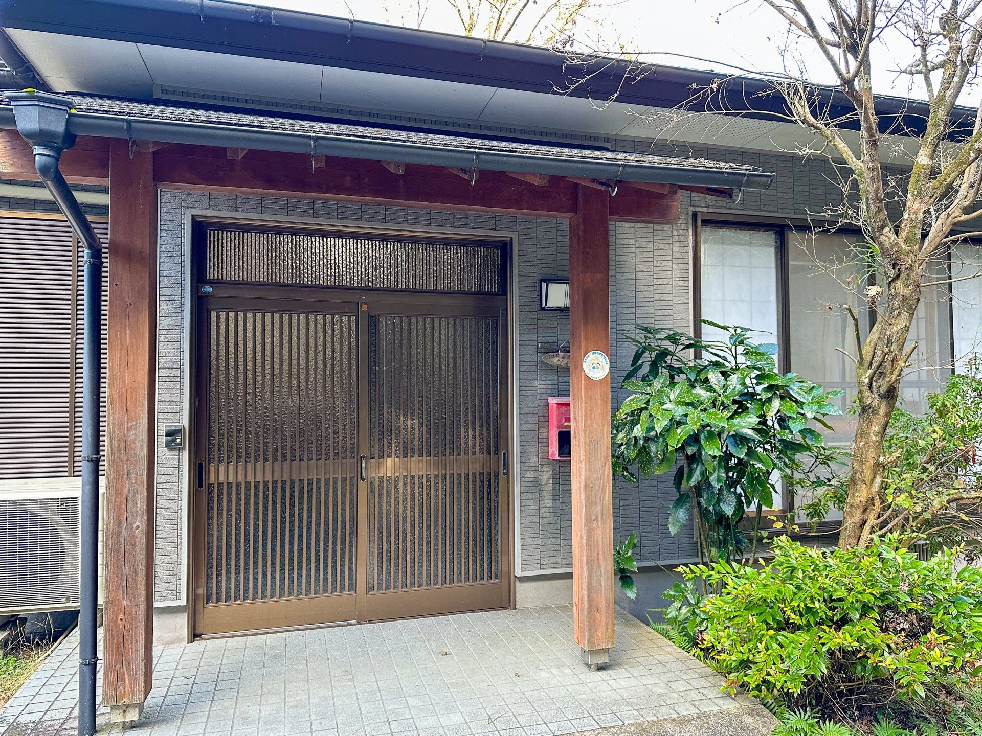 ブルーのエプロンを付けた若い女性スタッフに付き添われて笑顔で散歩をしているブラウンのジャケットを着た高齢女性。
