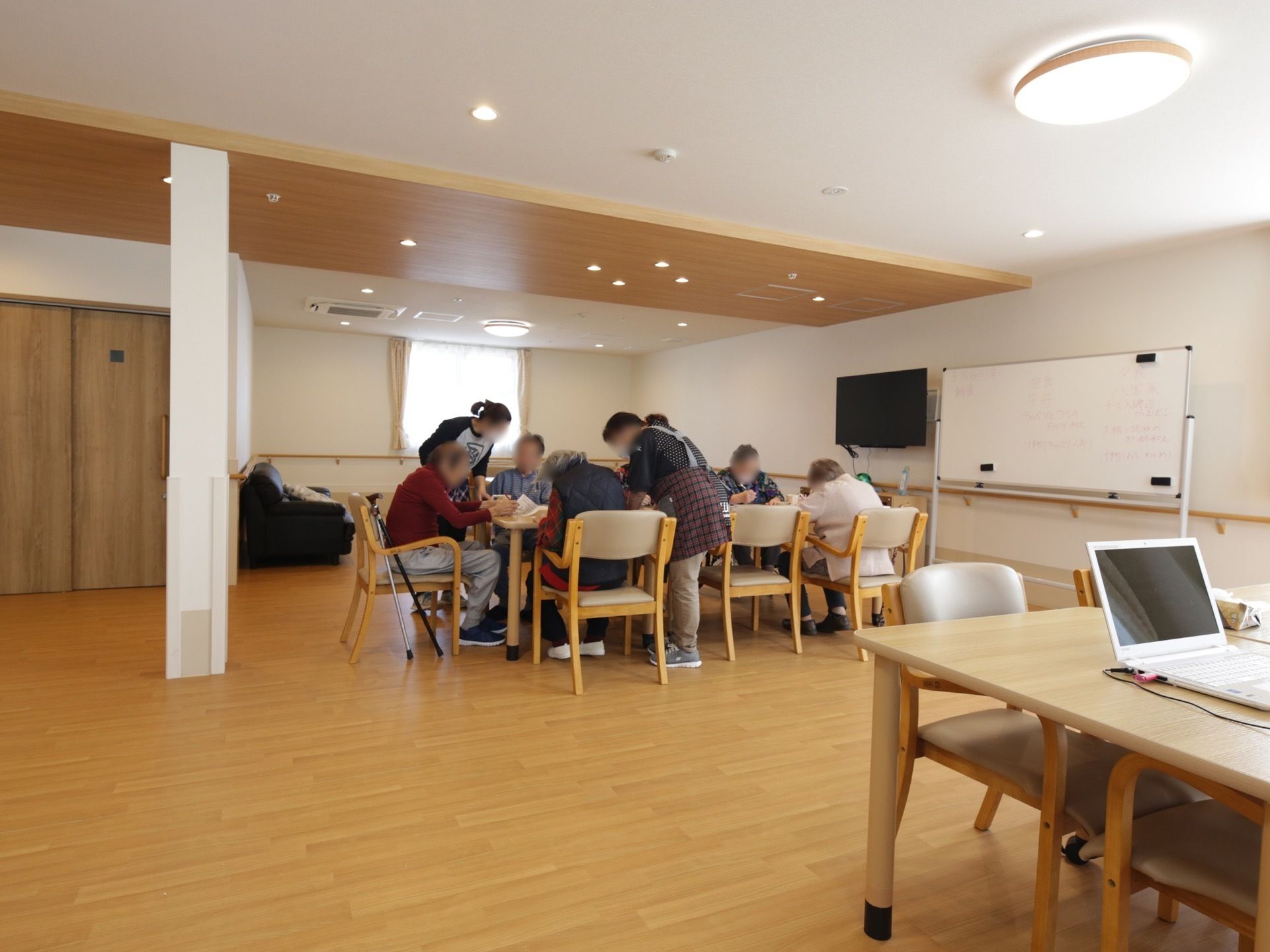 広々としたデイルームでは、入居者とスタッフが集まって活動している。ホワイトボードやテレビがあり、さまざまな活動が行える設備が整っている。
