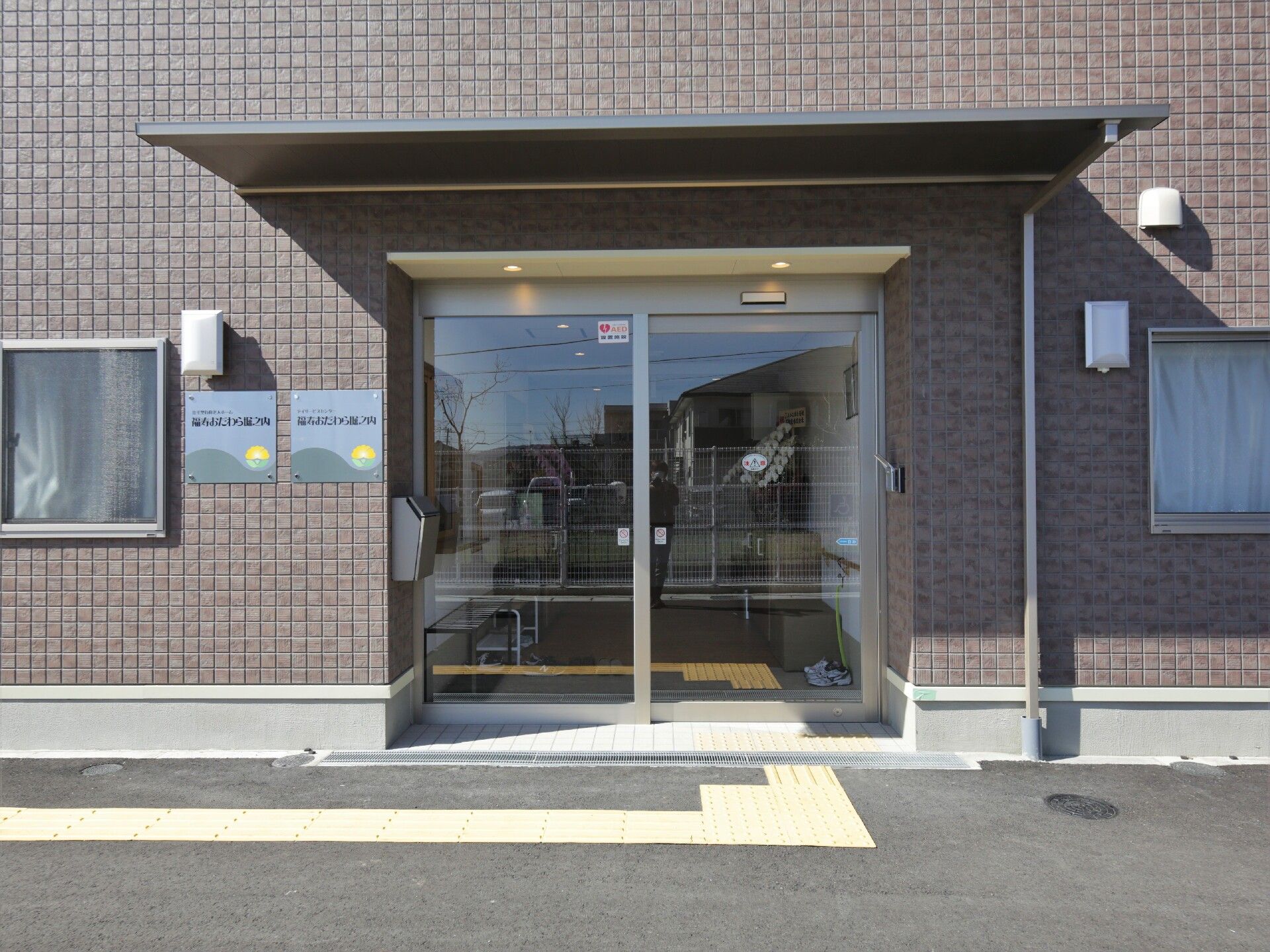 エル字型の建物は2階建てで1階部分はブラウン、2階部分はベージュ。青い空が広がっている。
