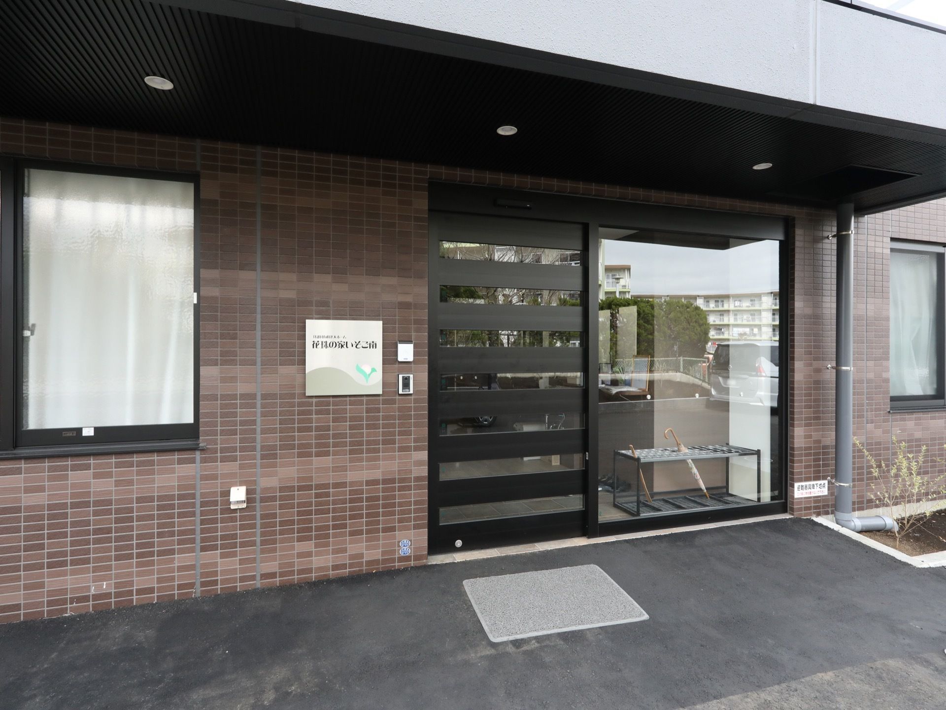 外壁はシックなブラウンで施されており、施設名が記された看板とインターホンが設置されている。入口は自動扉である。