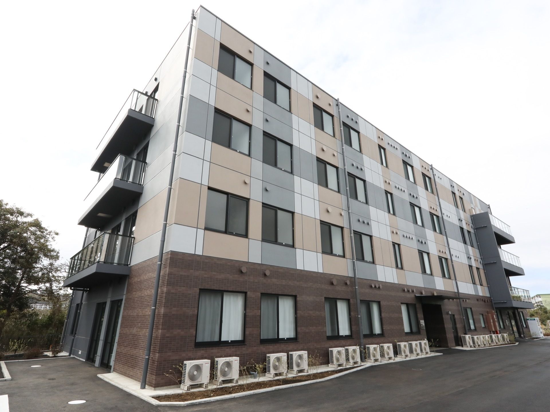 施設は４階建ての建物である。１階部分にはエアコンの室外機が設置されている。敷地内はアスファルトで舗装されている。