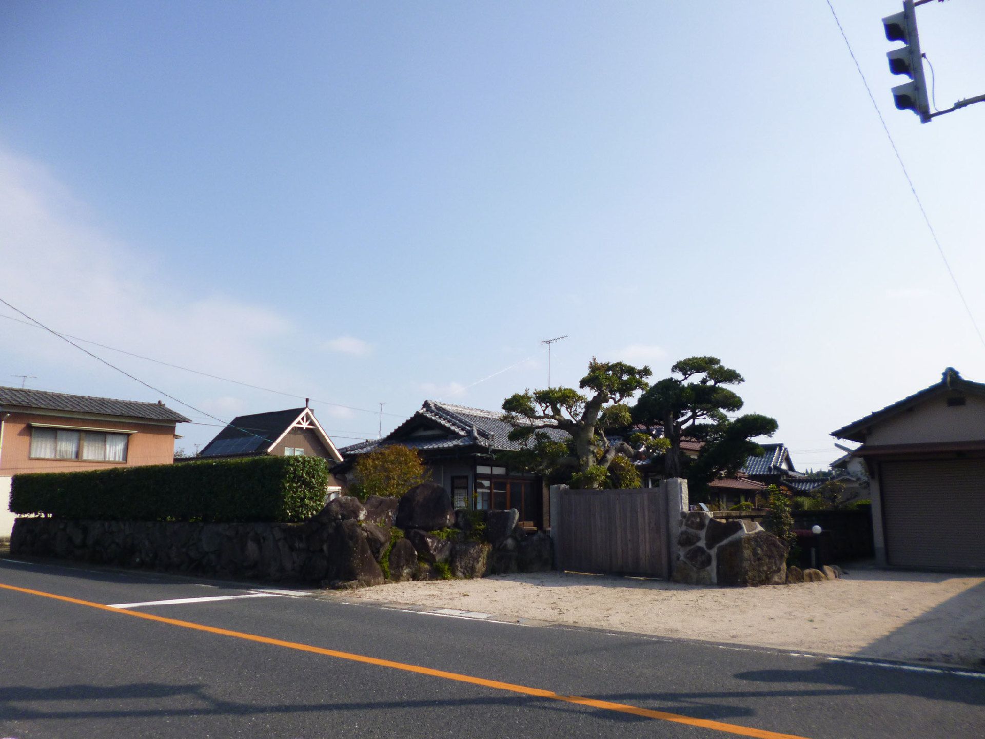 瓦屋根の和風の住居には庭が付き、すぐそばに数件の住宅が建っている。